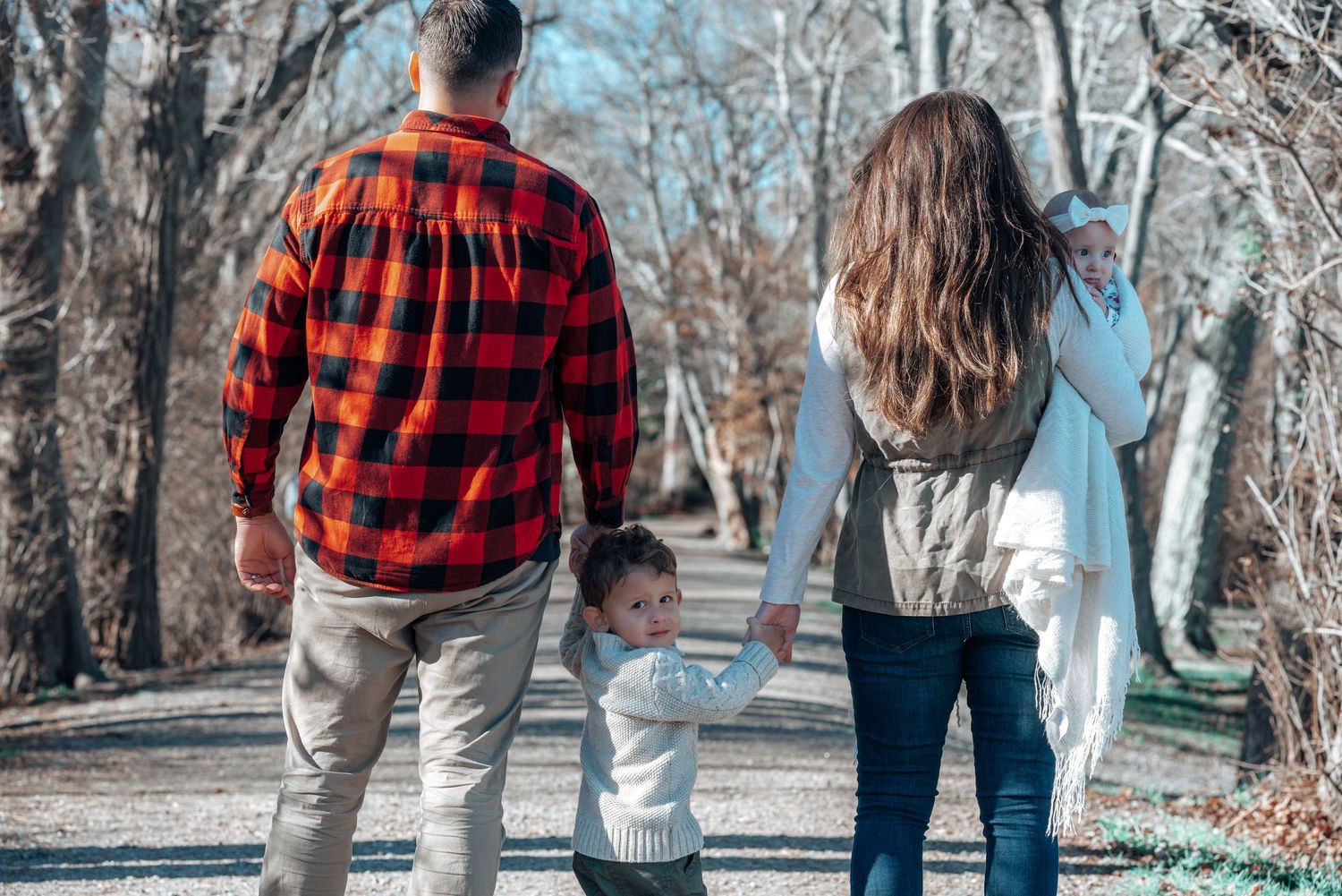 Family holding hands while walking together on a wooded path in autumn.
