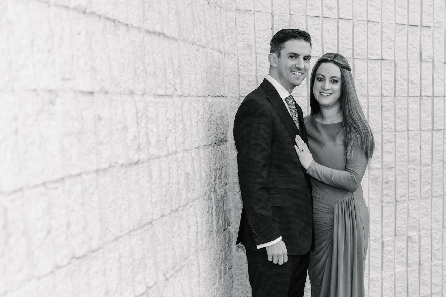 A black and white portrait of a couple against a textured wall.