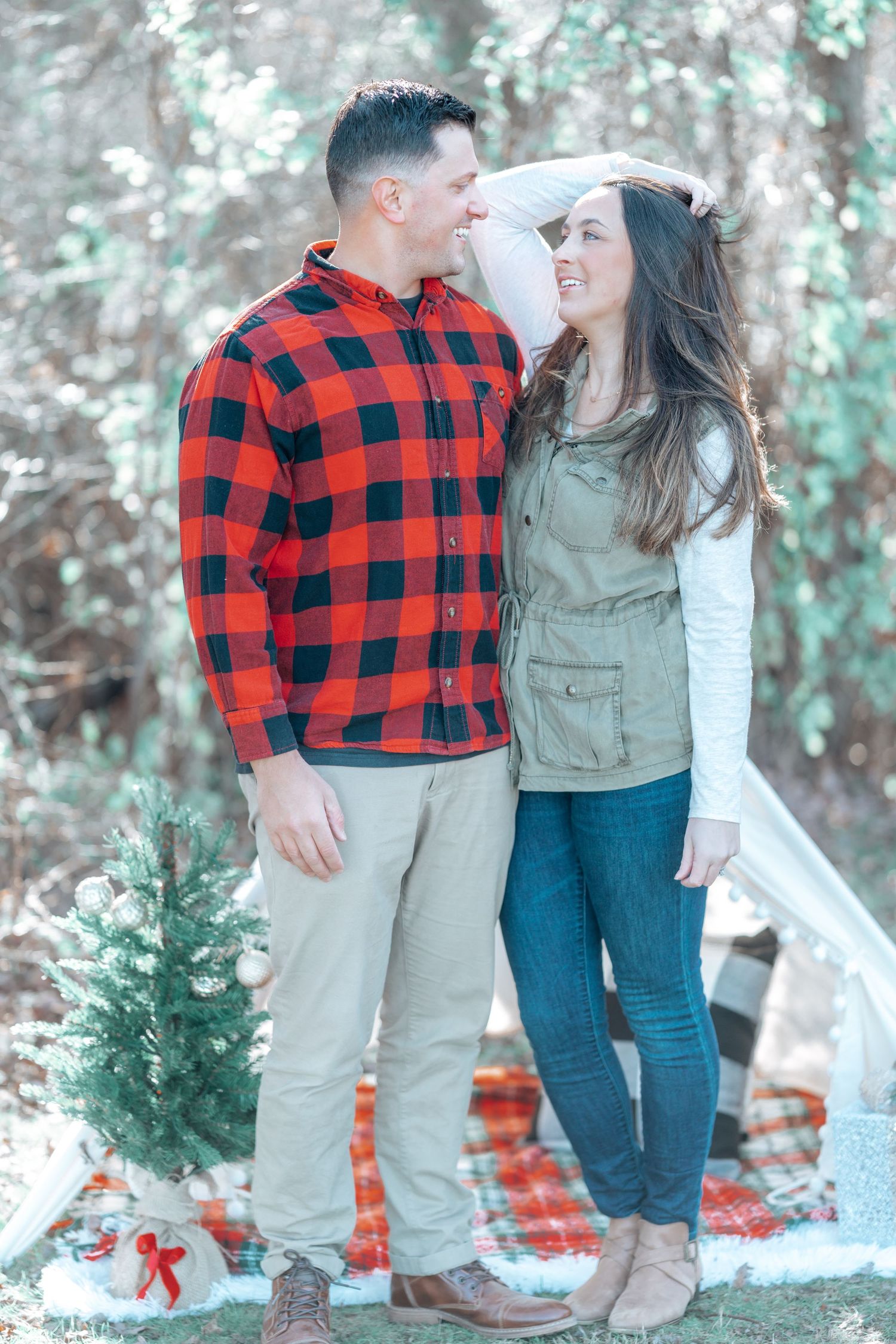 Couple in coordinated outfits standing by a white teepee and small Christmas tree.