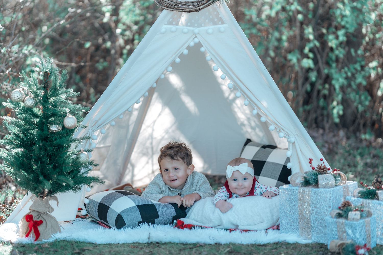 Two children relaxing in a white teepee tent with holiday decorations.