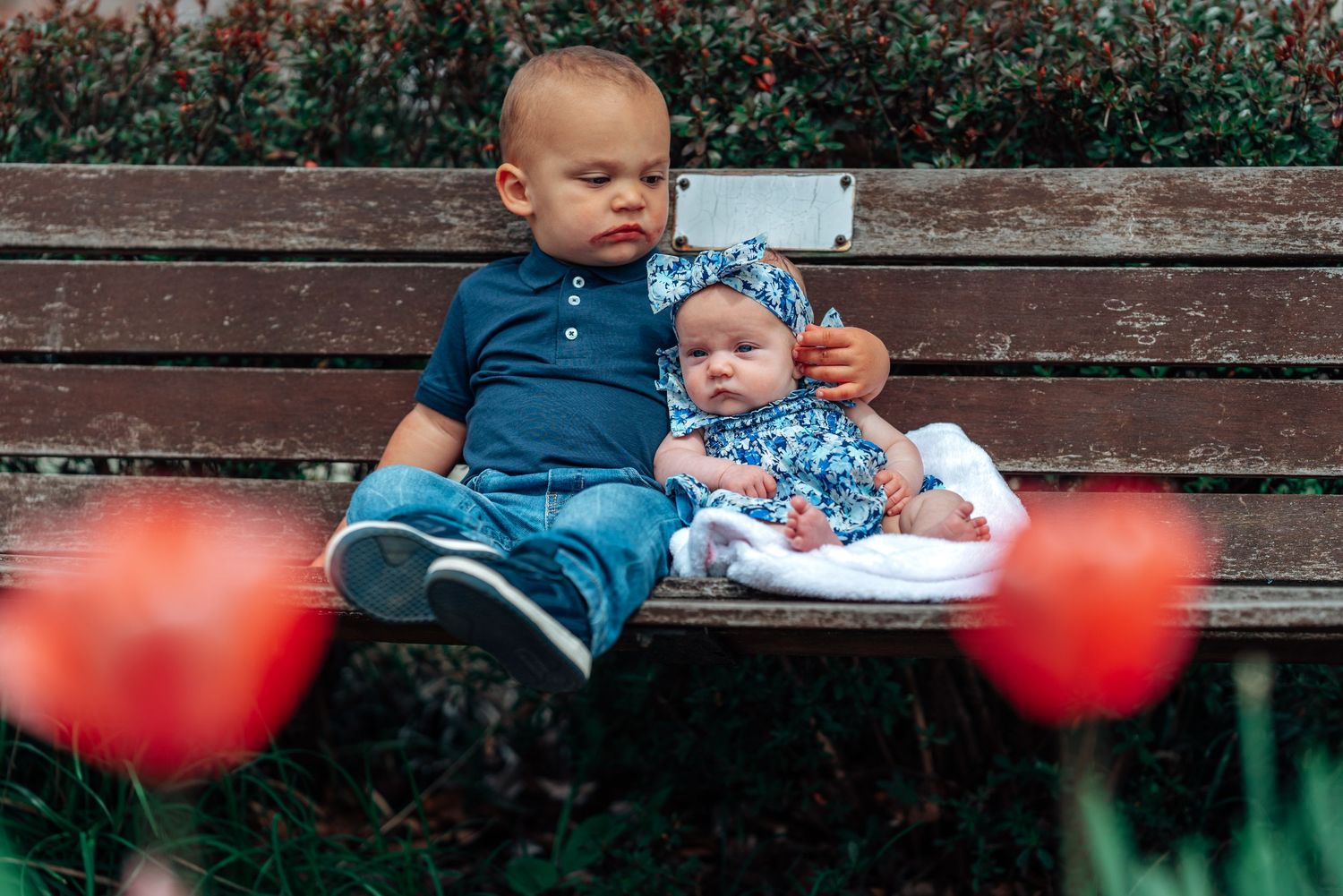 Two young children sitting on a wooden bench with pink tulips blooming in the foreground.