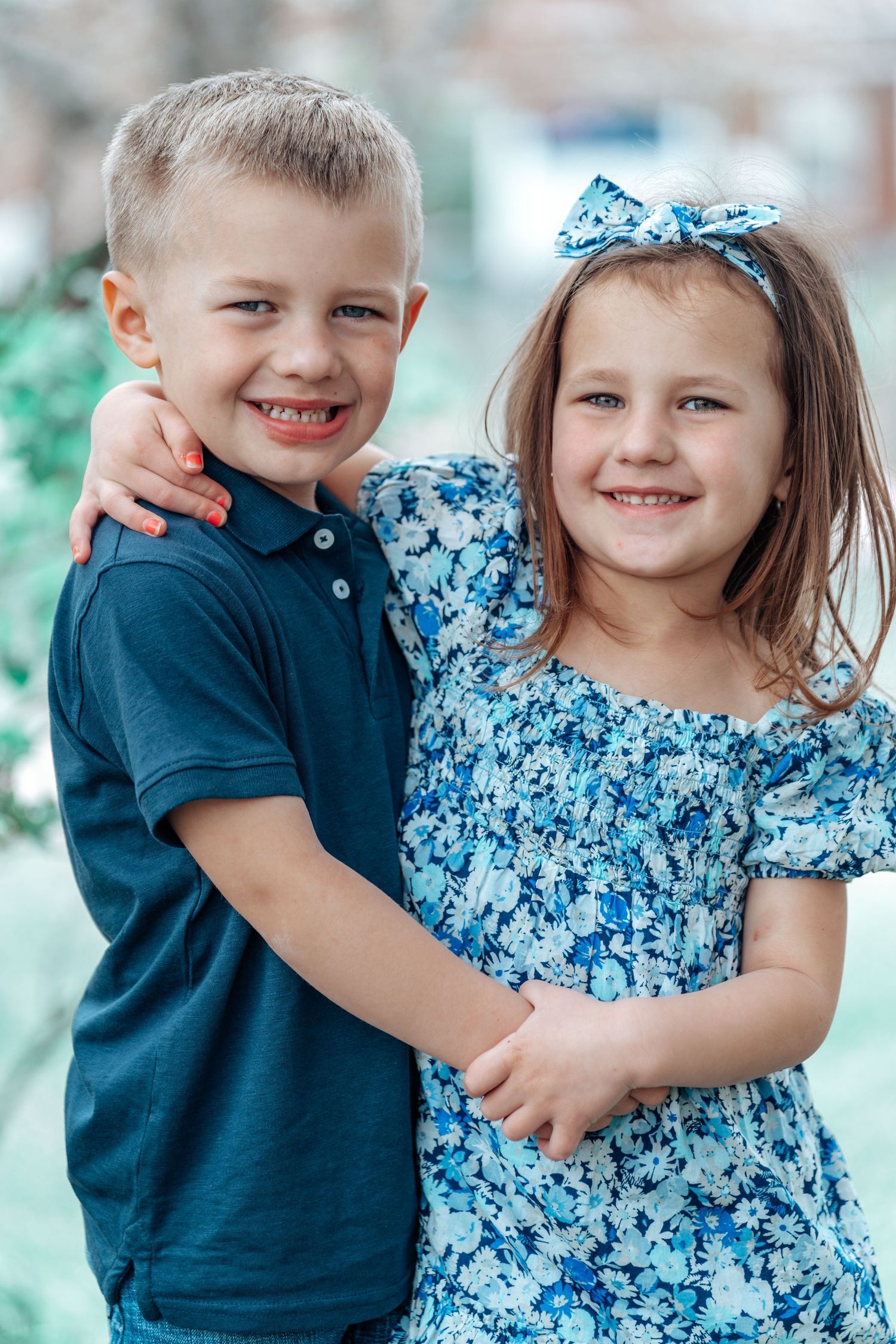 Two young children in coordinating blue outfits share a sweet embrace while posing together.