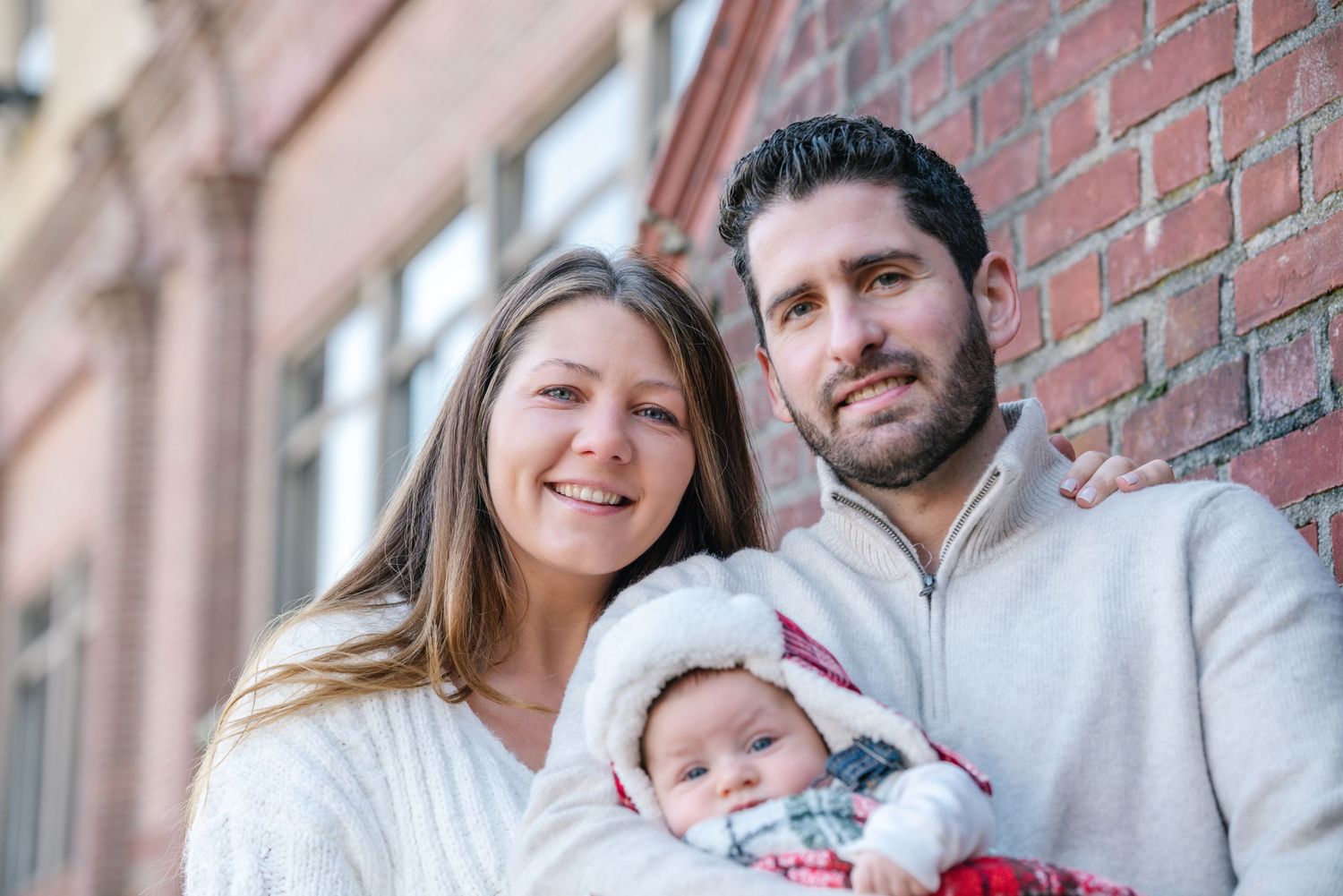 Cozy winter family portrait against a brick building backdrop.