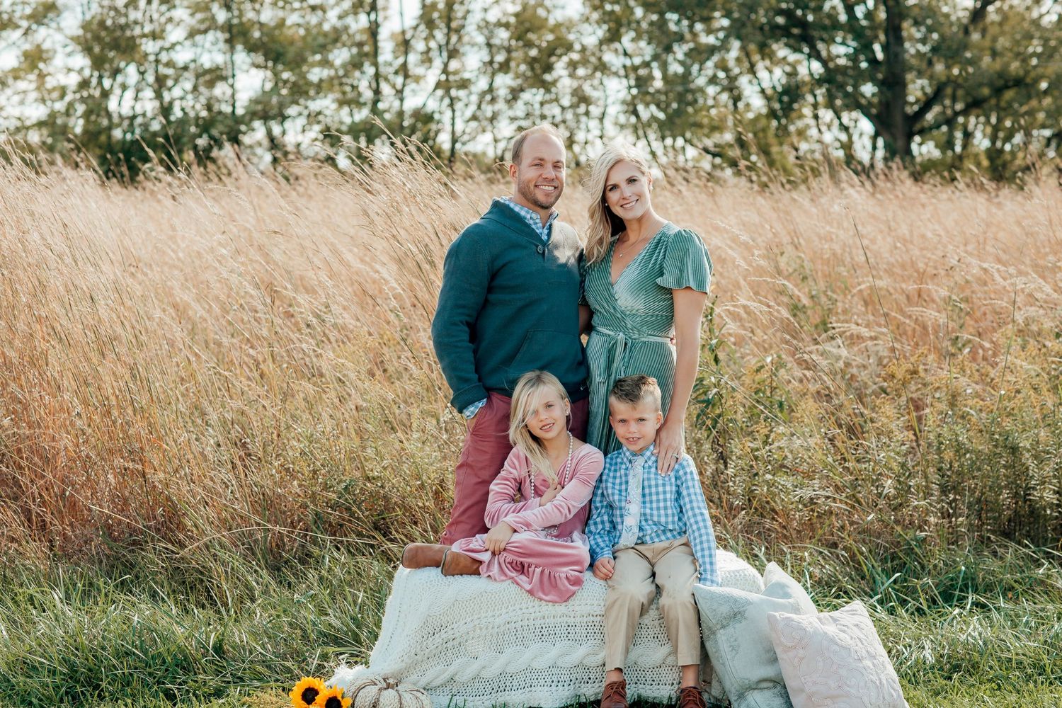 Family having picnic together in tall autumn grass during golden hour.