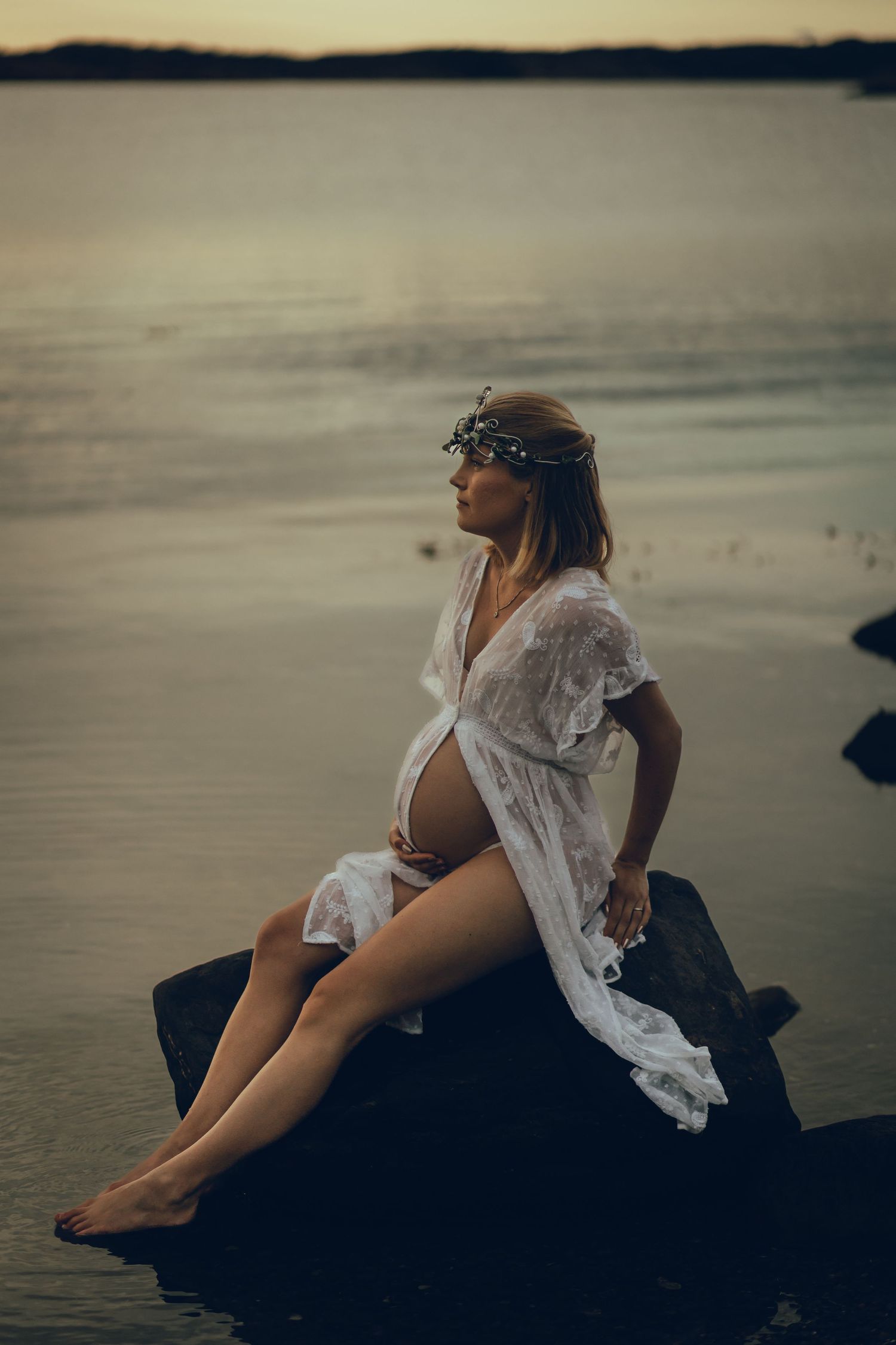 Gravid kvinna sitter på en sten i havet med sagokrona på huvudet