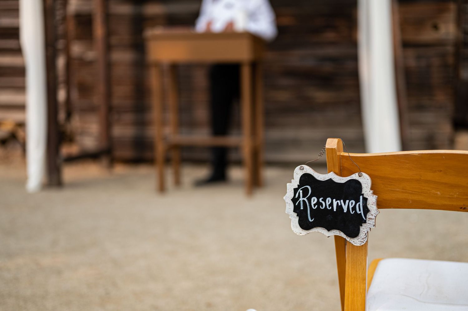 A wooden chair at a wedding ceremony with a small chalkboard reserved sign.