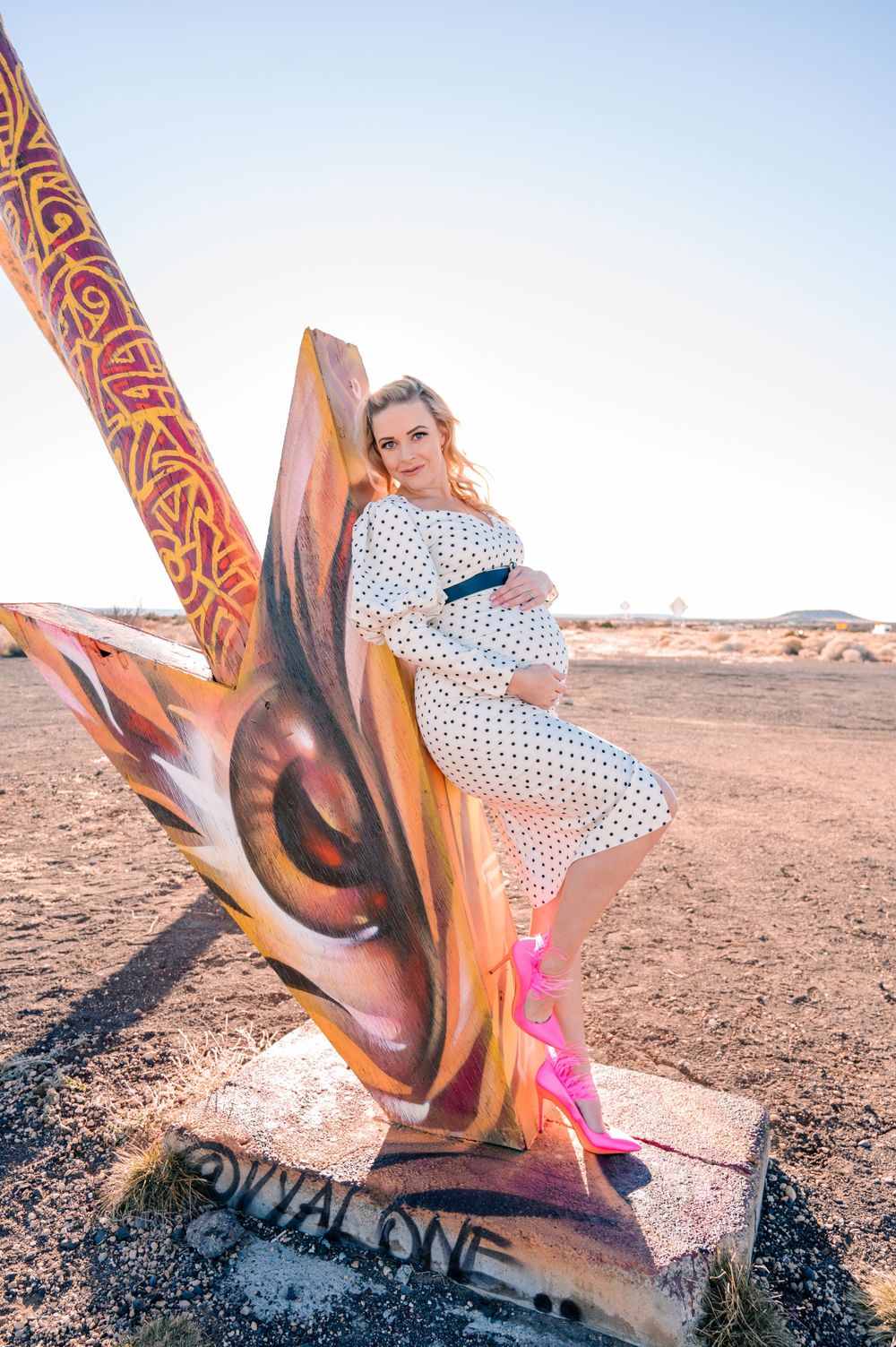 A polka dot dress and bright pink heels contrast against desert scenery and colorful street art.