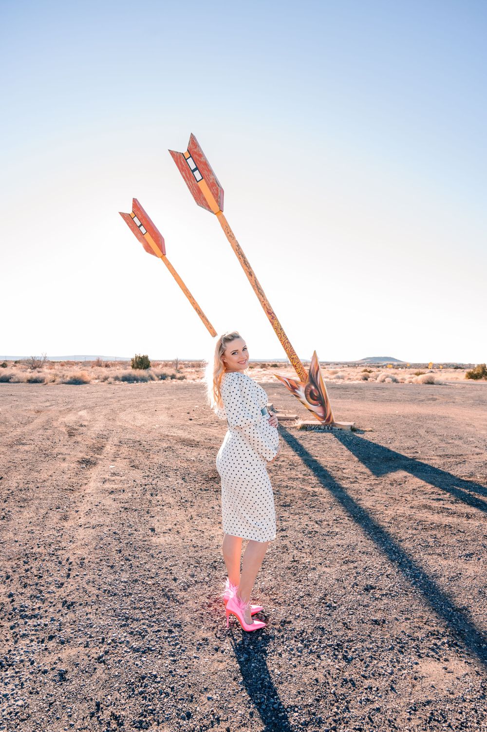 A desert fashion shoot with large decorative arrows and bright pink shoes.
