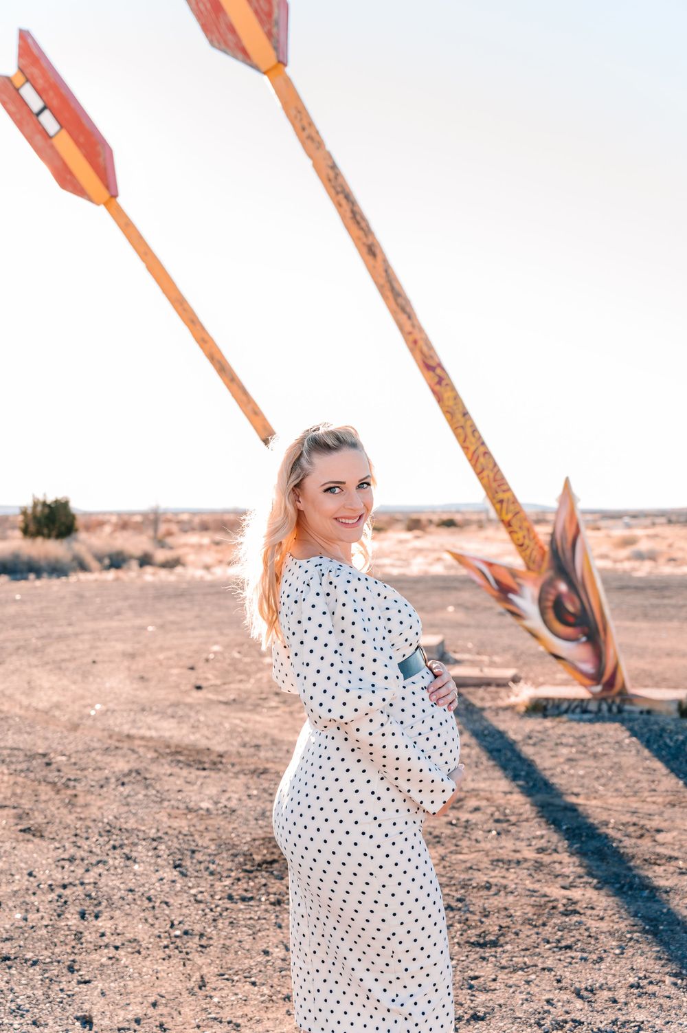 A maternity photoshoot in a desert setting with large wooden arrow sculptures.