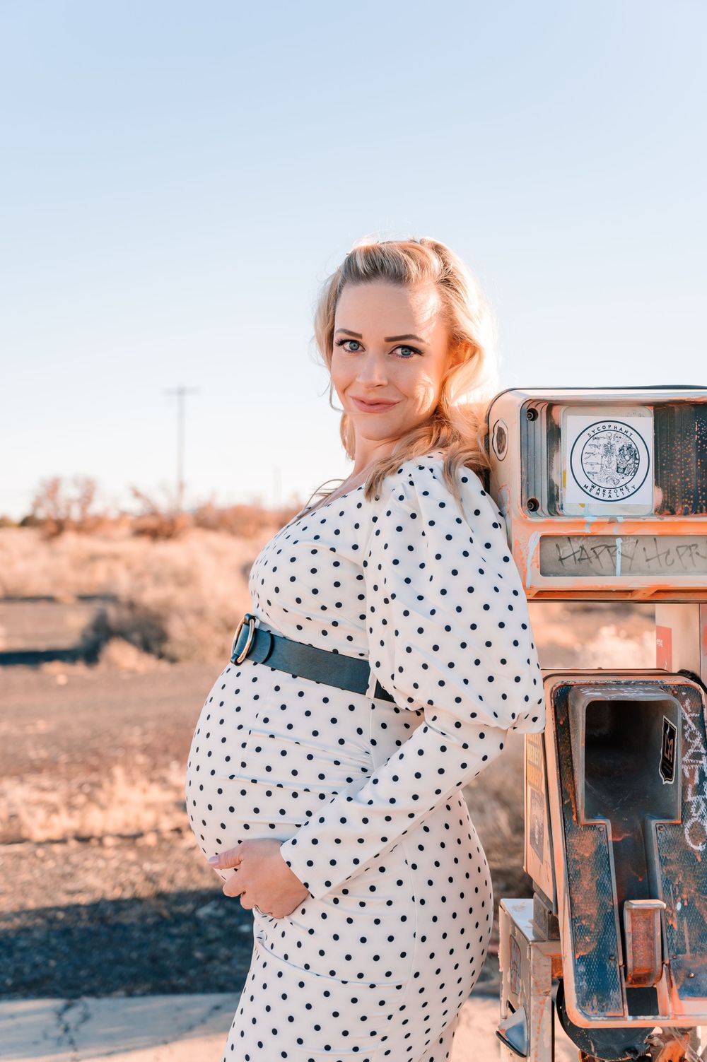 A retro-inspired maternity photo next to a rustic gas pump in the desert.