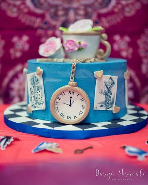 Alice in Wonderland themed cake with pocket watch and teacup decorations on checkered base.