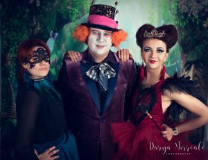 Fantastical group portrait with colorful costumes and masks against enchanted forest backdrop.