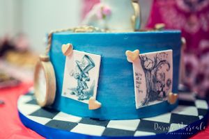 Close-up of a blue Alice in Wonderland themed cake with illustrated storybook panels and decorative details.