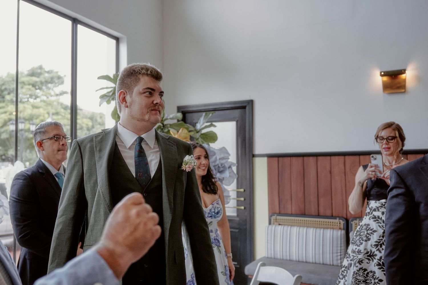 A formal gathering in a bright indoor space with attendees standing and watching.