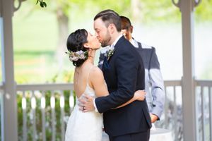 Bride and groom share first kiss at outdoor gazebo wedding ceremony with officiant nearby.