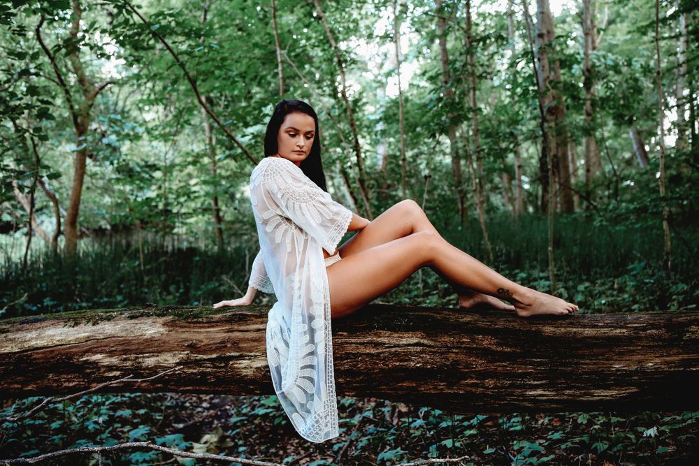 Artistic portrait session on fallen log in lush green forest setting.