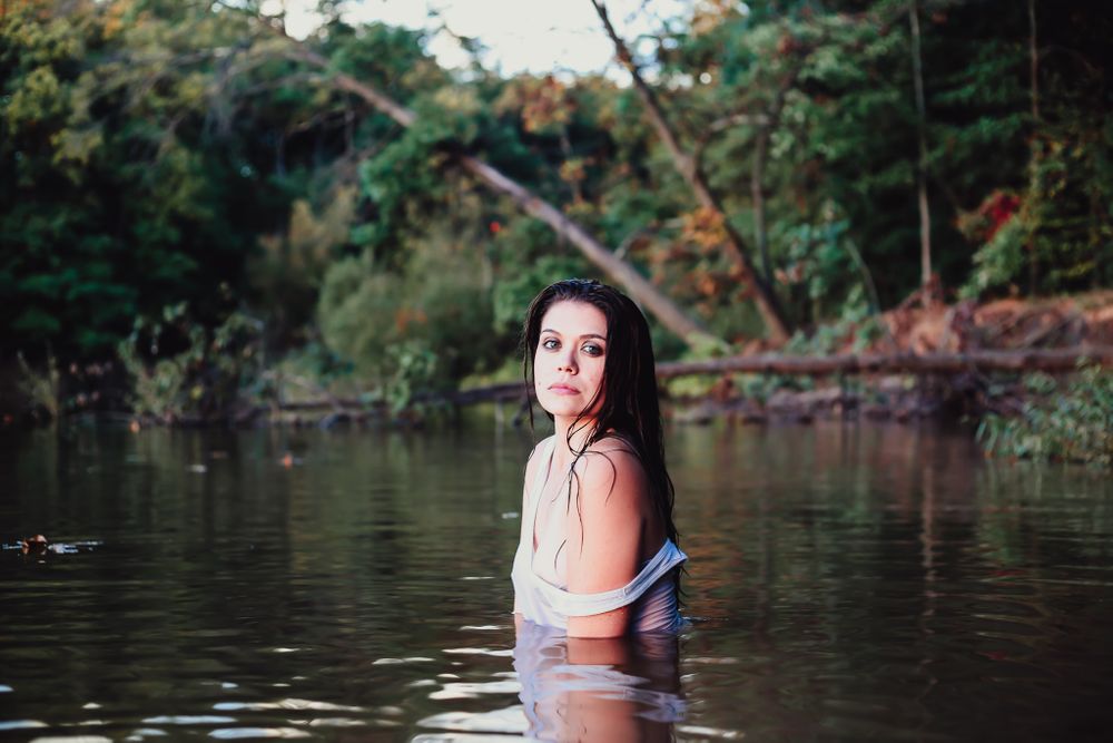 Woman in water against lush green foliage during golden hour photography session.