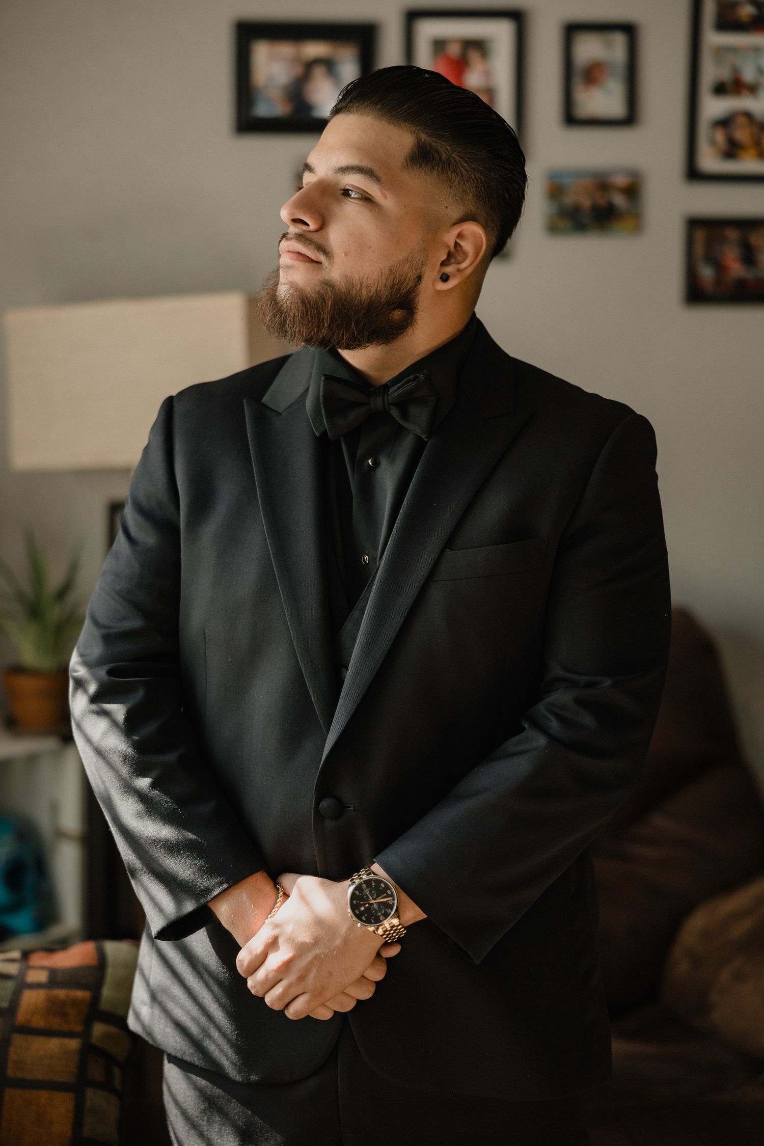A formal portrait in a black suit and tie against an interior background with photo frames.