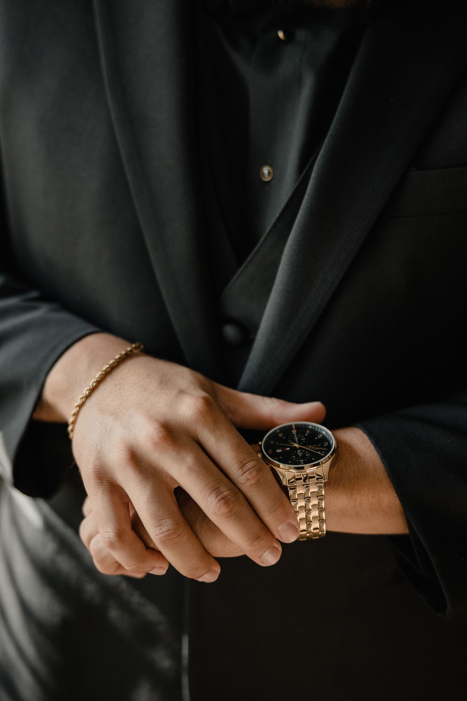 Close-up detail of a gold watch worn with a black formal suit.