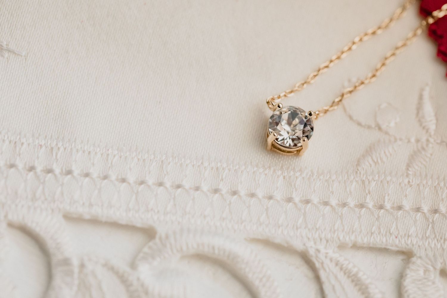 A delicate crystal pendant necklace on a gold chain against white fabric.