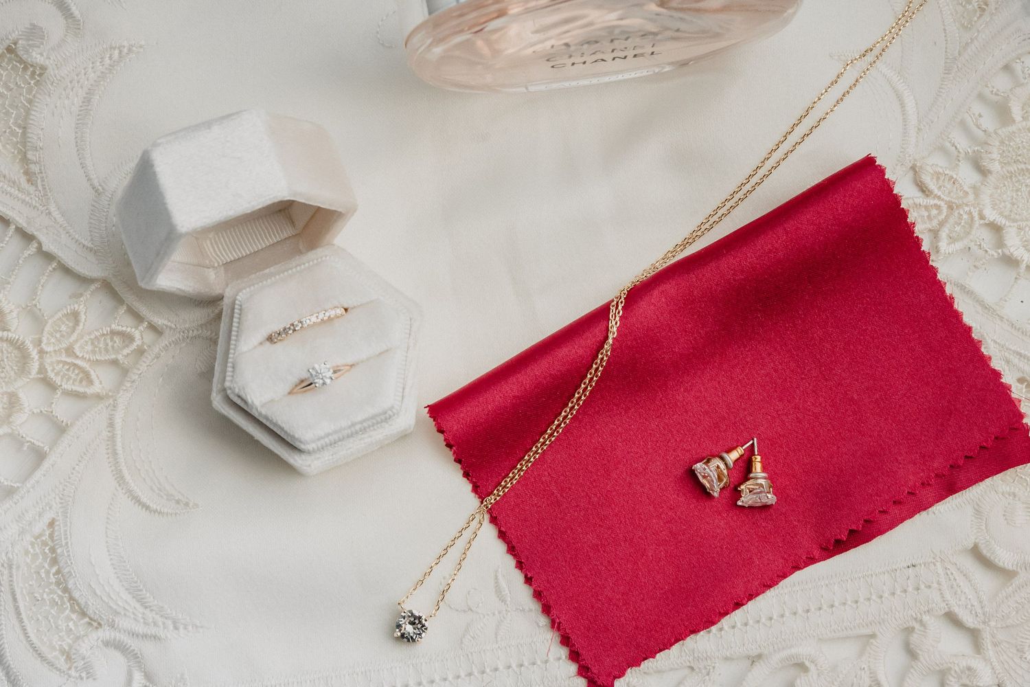Wedding accessories including jewelry and a red velvet pouch arranged on white lace fabric.