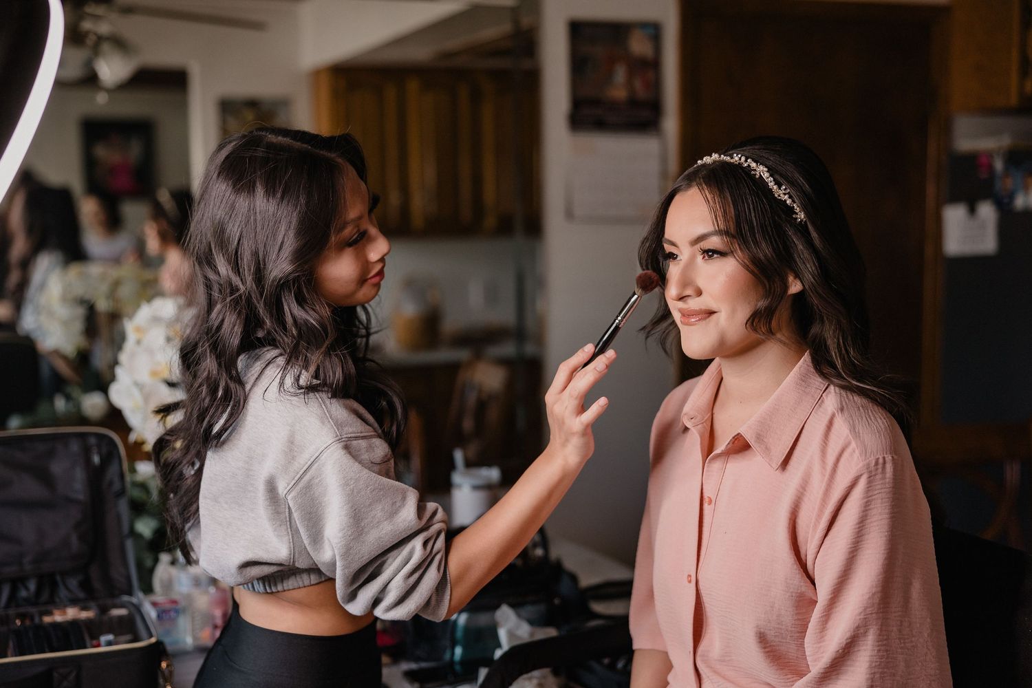 Makeup artist applying cosmetics to a client wearing a peach colored blouse during wedding preparations.