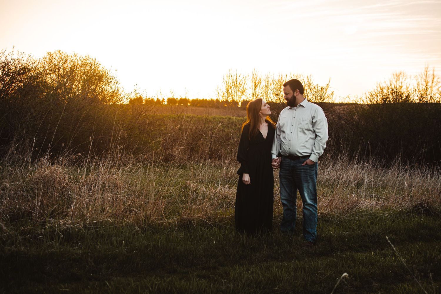 Silhouetted couple standing in golden field during sunset.