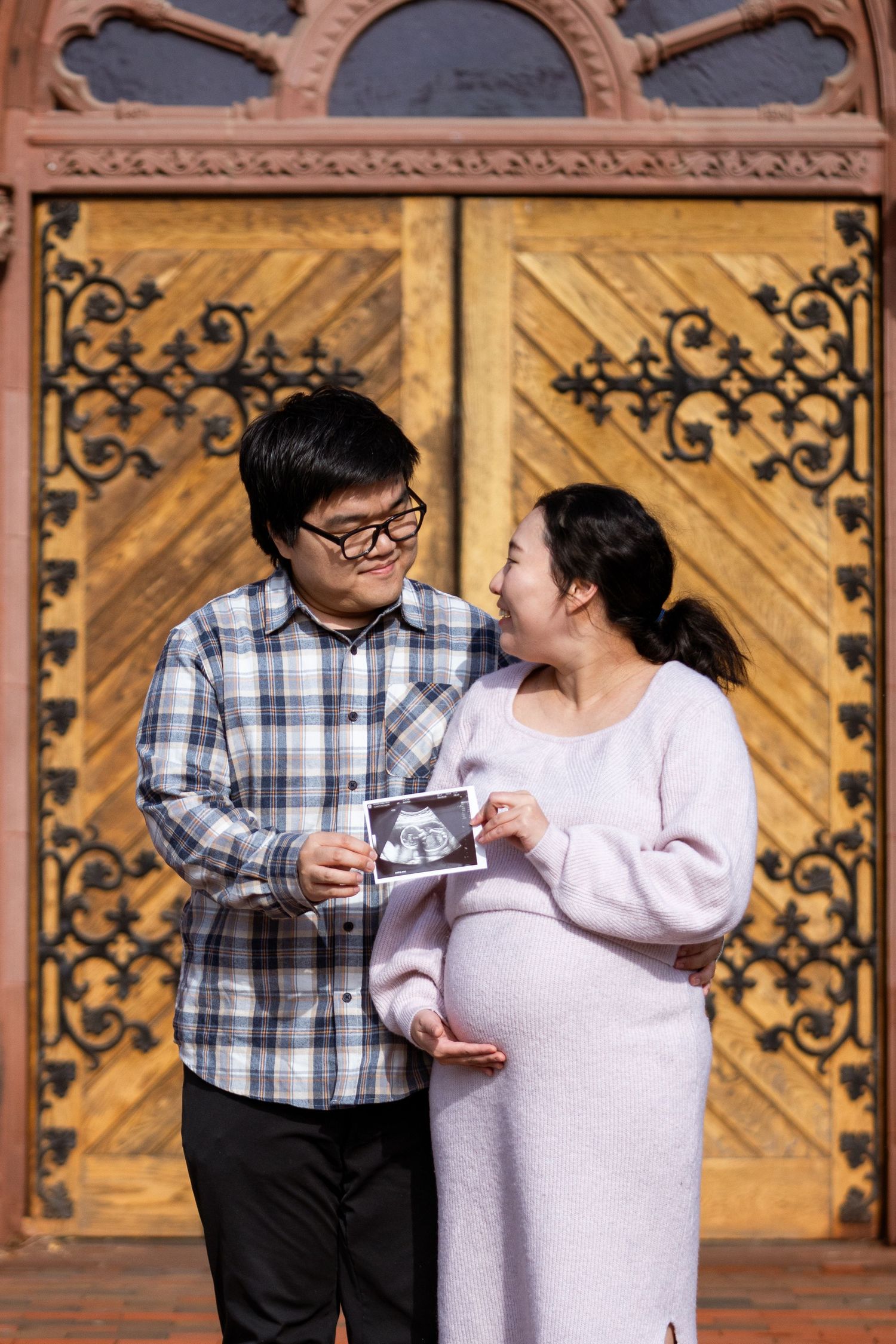 A couple dances together in front of ornate wooden doors with decorative patterns.