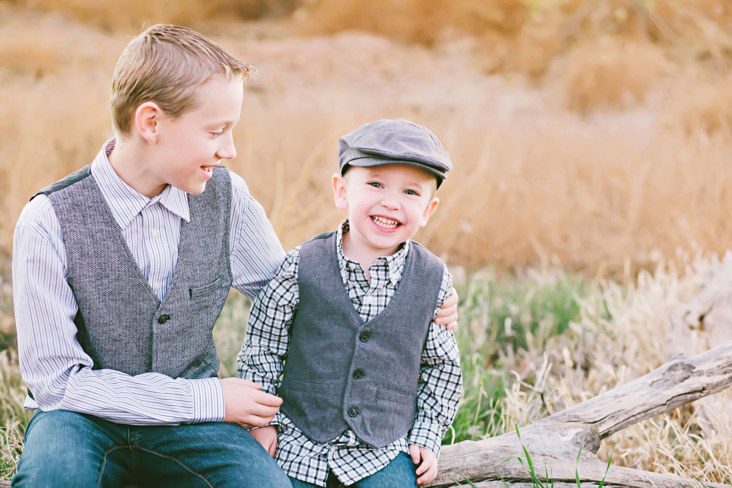 Parent and child sitting on log laughing together in golden field during sunset.