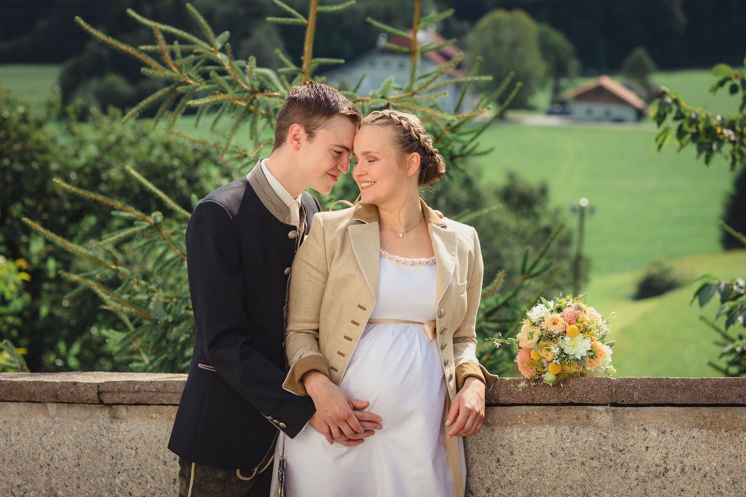 A romantic couple embraces on a balcony overlooking lush mountain scenery.