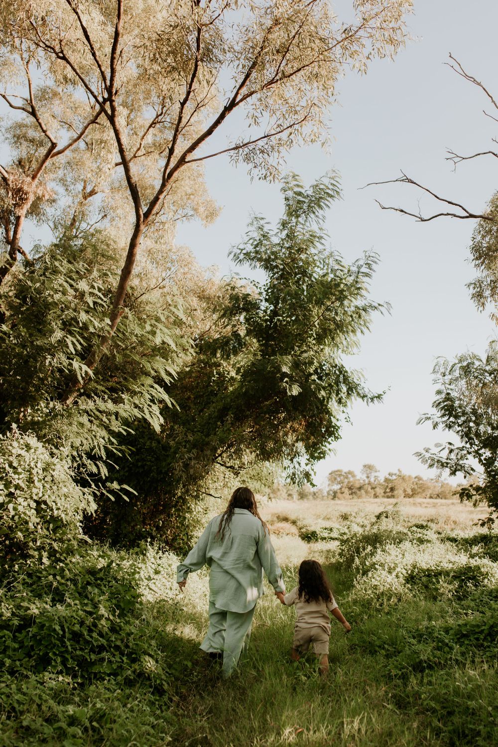 Wide shot of mother and sun walking through green grass in Mount Isa