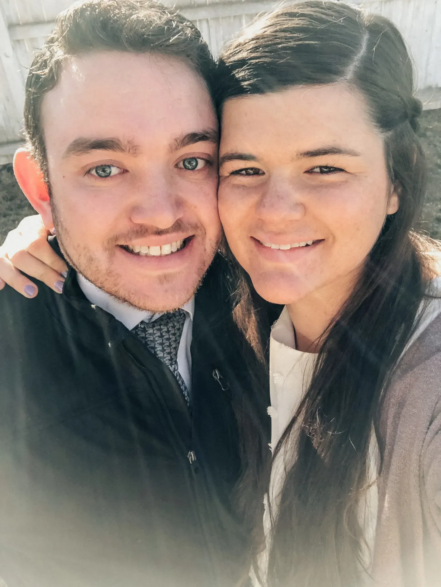 A close-up selfie of two people smiling at the camera on a sunny day.