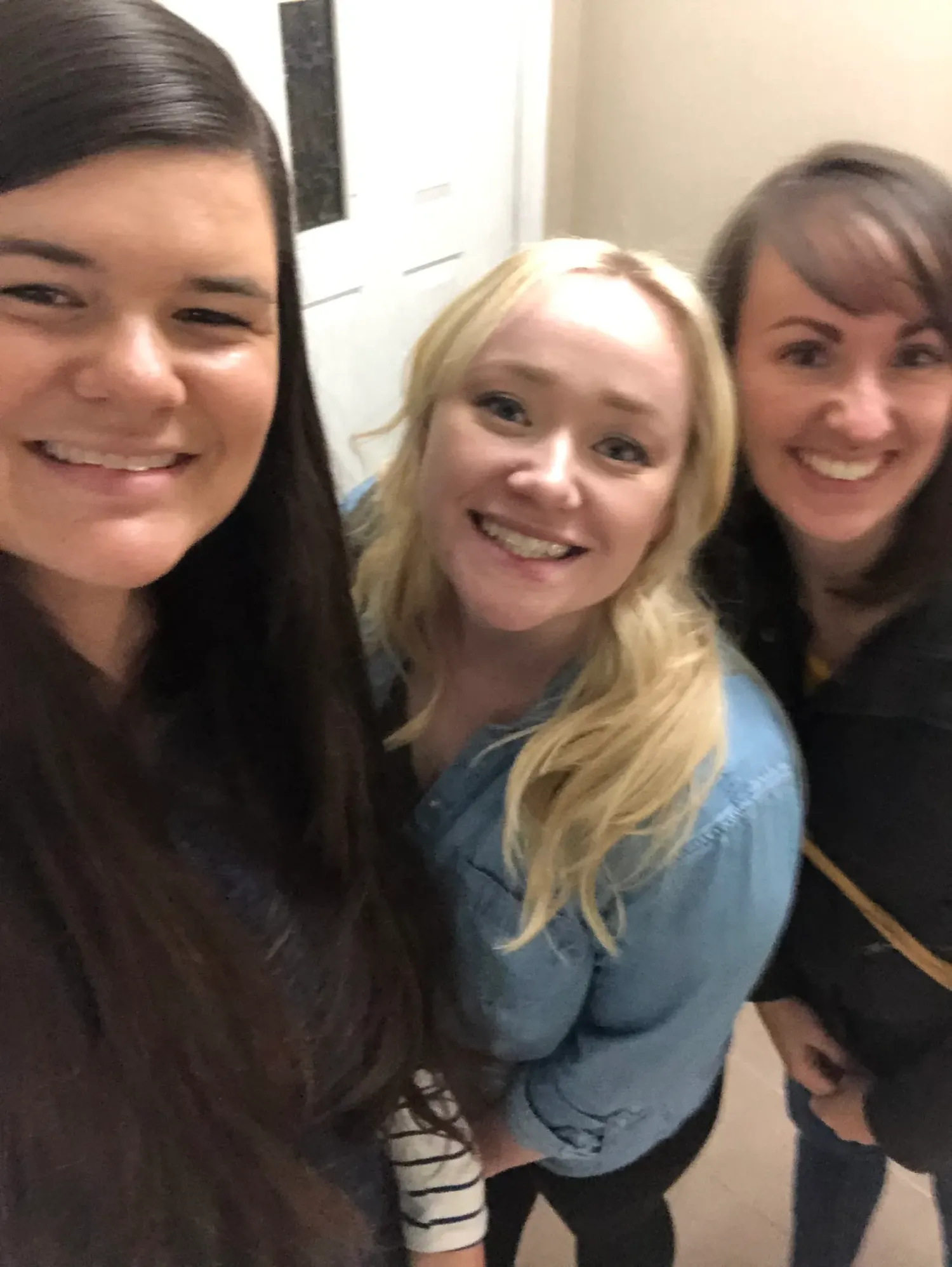 Three friends pose together for a casual indoor selfie.