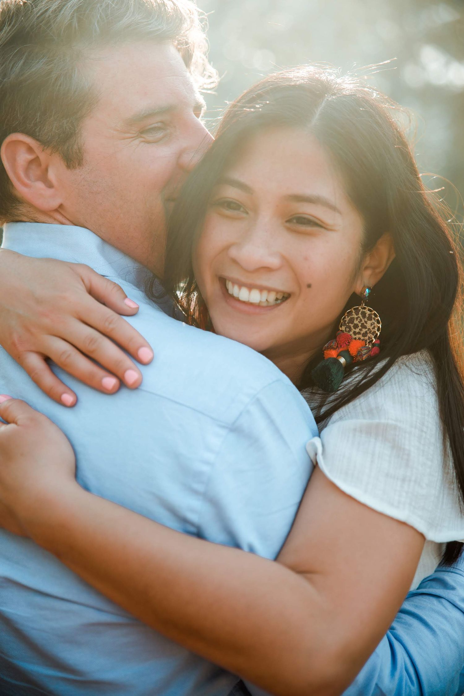 A joyful couple shares a loving embrace outdoors with golden sunlight filtering through trees.