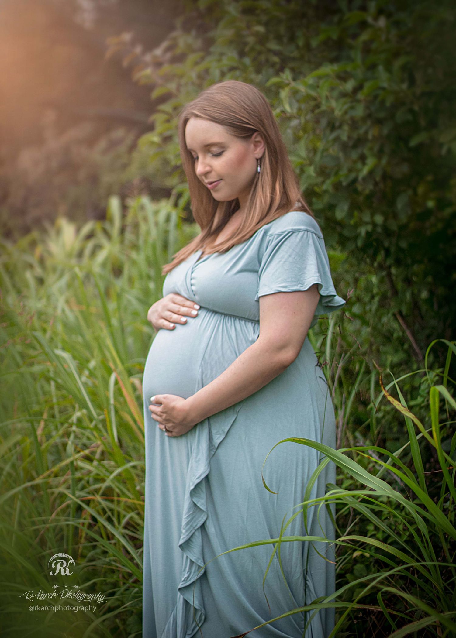 Maternity portrait of an expectant mother in a flowing blue dress amidst tall grass at golden hour.
