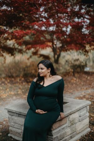 Maternity photos by stone wall with vibrant red autumn foliage in background.