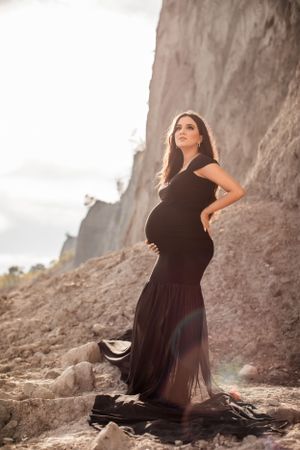 Dramatic maternity portraits against towering coastal cliffs in a black dress.
