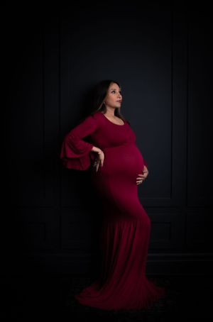 Artistic maternity photos showing silhouette poses in burgundy dress against dark backdrop.