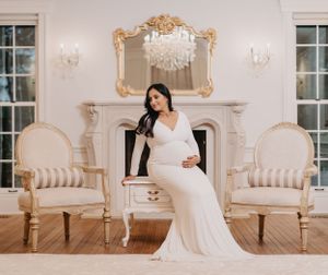 Elegant maternity photos in luxurious white room with ornate gold mirrors and chandeliers.