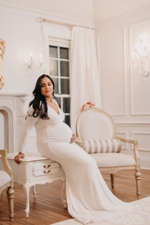 Maternity session in flowing white gown against classic French provincial interior design.