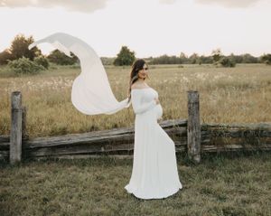A flowing white dress twirls gracefully in a rustic field with wooden fence posts at sunset.