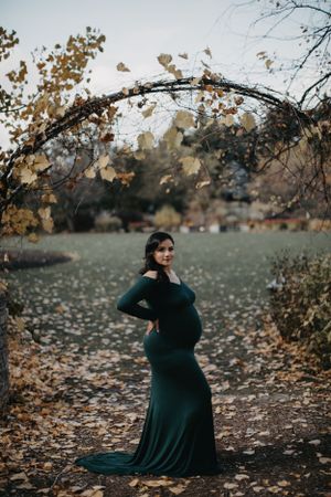 Autumn maternity session in park with fallen leaves and muted natural tones.