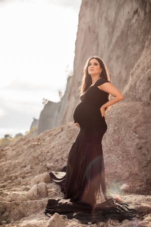 Woman in black dress poses elegantly near rocky cliffside during outdoor photo session.