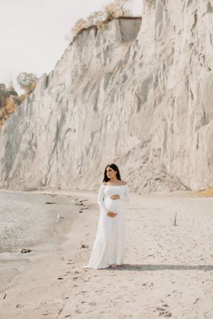 Ethereal beach maternity photos with white flowing dress against limestone cliffs.