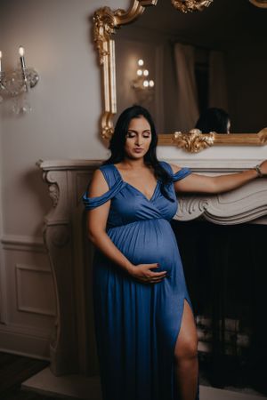 Moody maternity photography featuring navy blue dress in elegant room with fireplace.