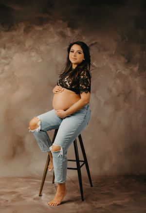 Studio maternity session featuring casual denim and natural poses on wooden stool.