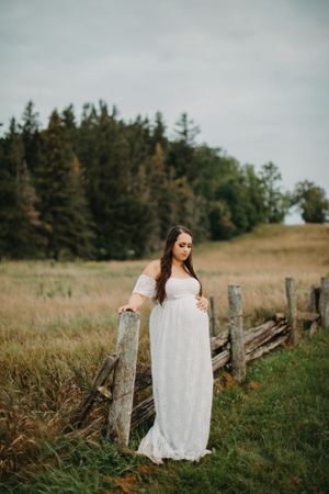 White lace dress photographed against rustic wooden fence in countryside field.
