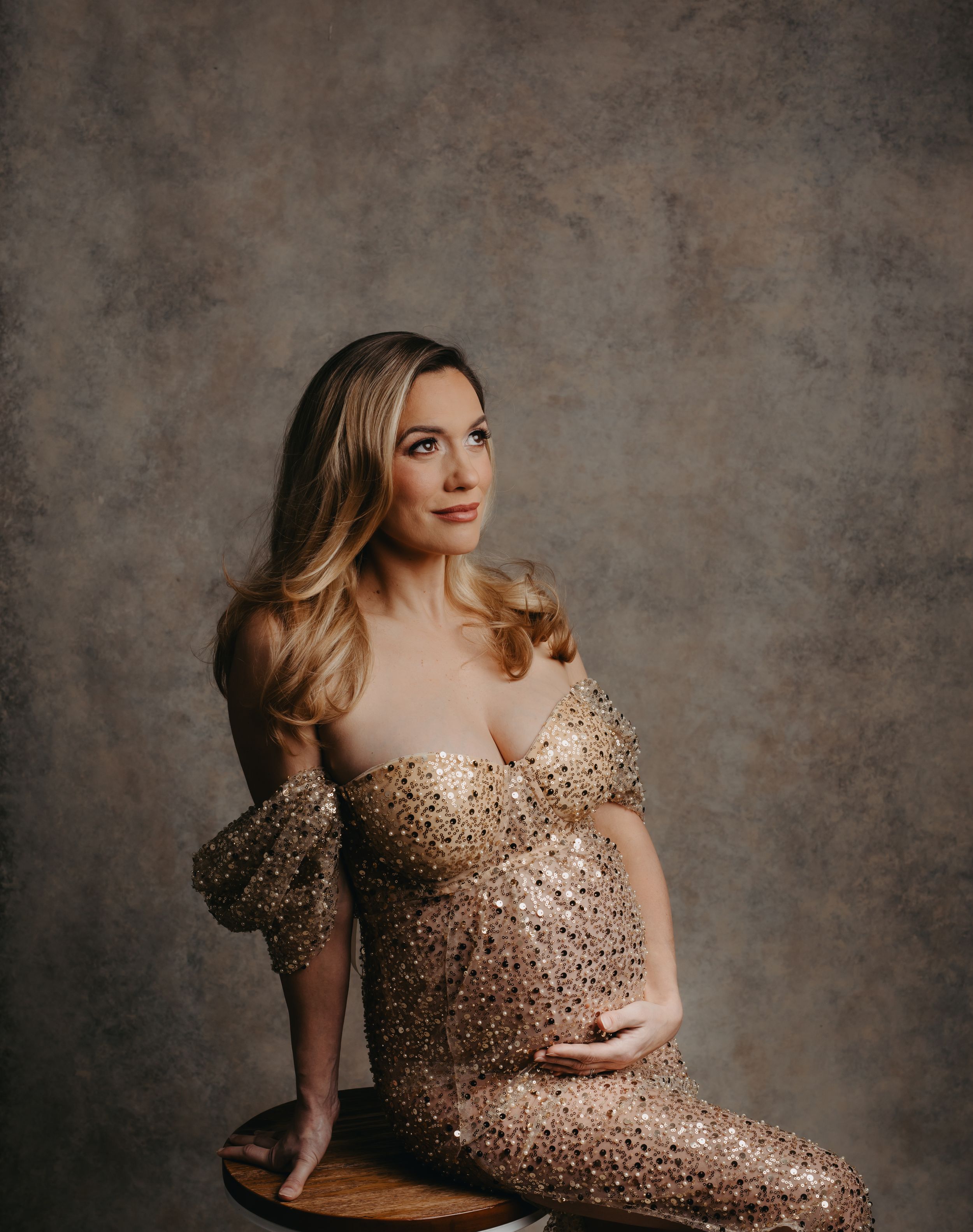 Woman in sparkly gold sequin dress poses elegantly against textured grey background.