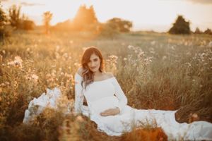 Expectant couple shares tender moments in sunlit meadow during sunset photoshoot.