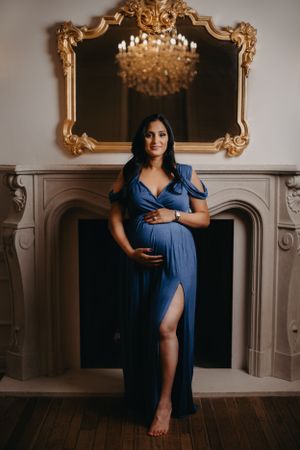 Dramatic maternity portraits in navy blue gown with ornate gold-framed mirror backdrop.